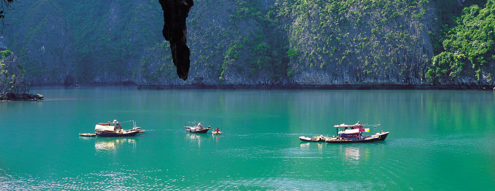 Båtar glider fram i turkosblått vatten i Halongbukten