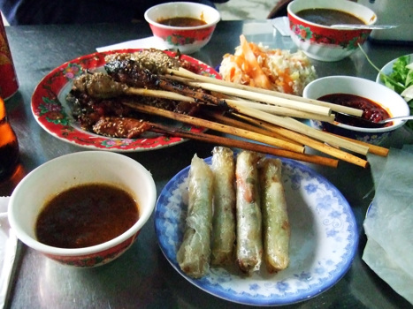 Tallrikar och skålar med mat och dippsås på ett bord med bordsskiva av kromad metall i staden Hoi An