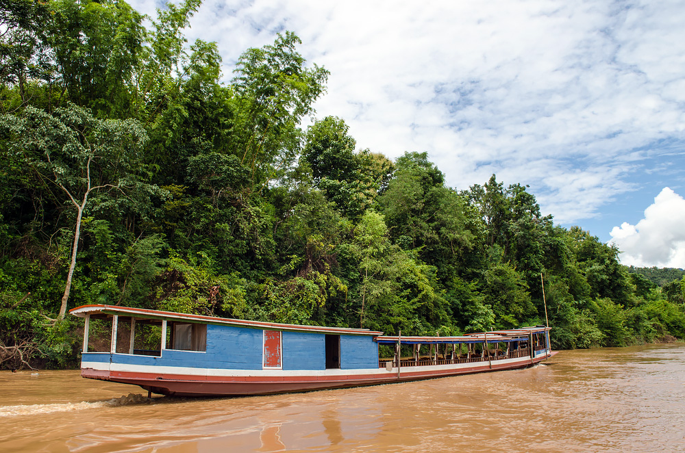 Blå flodbåt, brunt vatten med gröna träd i bakgrunden