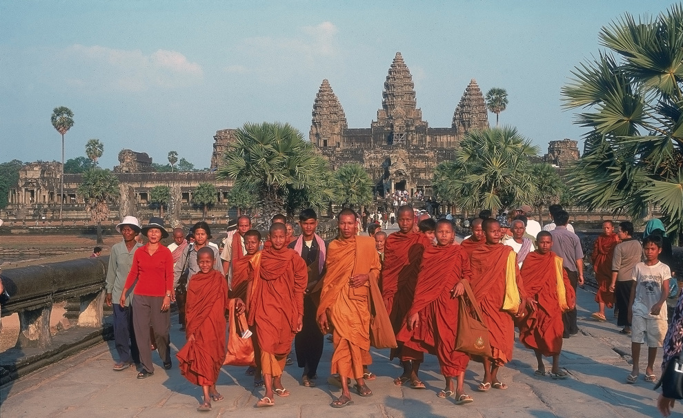 Orangeklädda munkar som går i bredd, tempel i bakgrunden