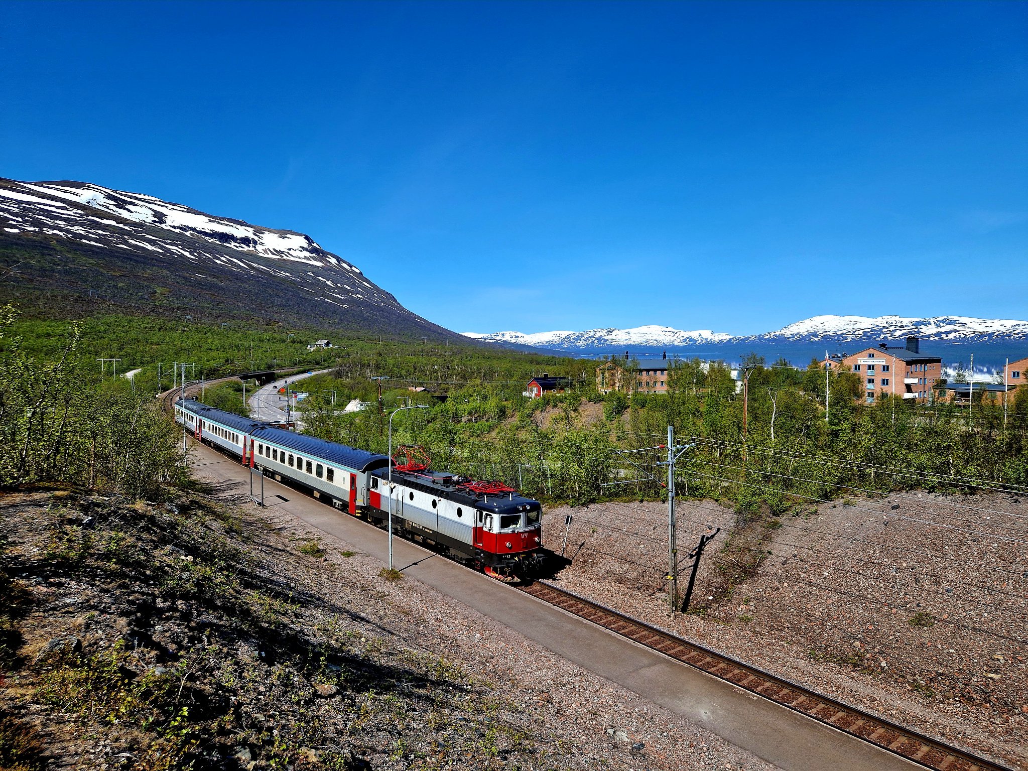 På bilden ser vi ett tåg som passerar Abisko Fjällstation i vackert landskap