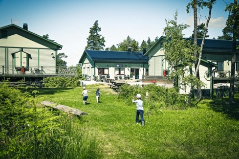 På bilden ser vi en grön äng framför Svartsö Skärgårdshotell och Vandrarhem