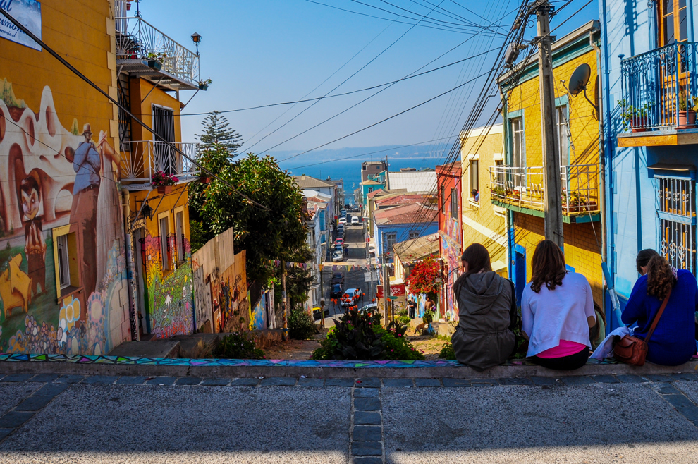 Personer sitter i trappa på en gata med färgglada hus i Valparaiso.