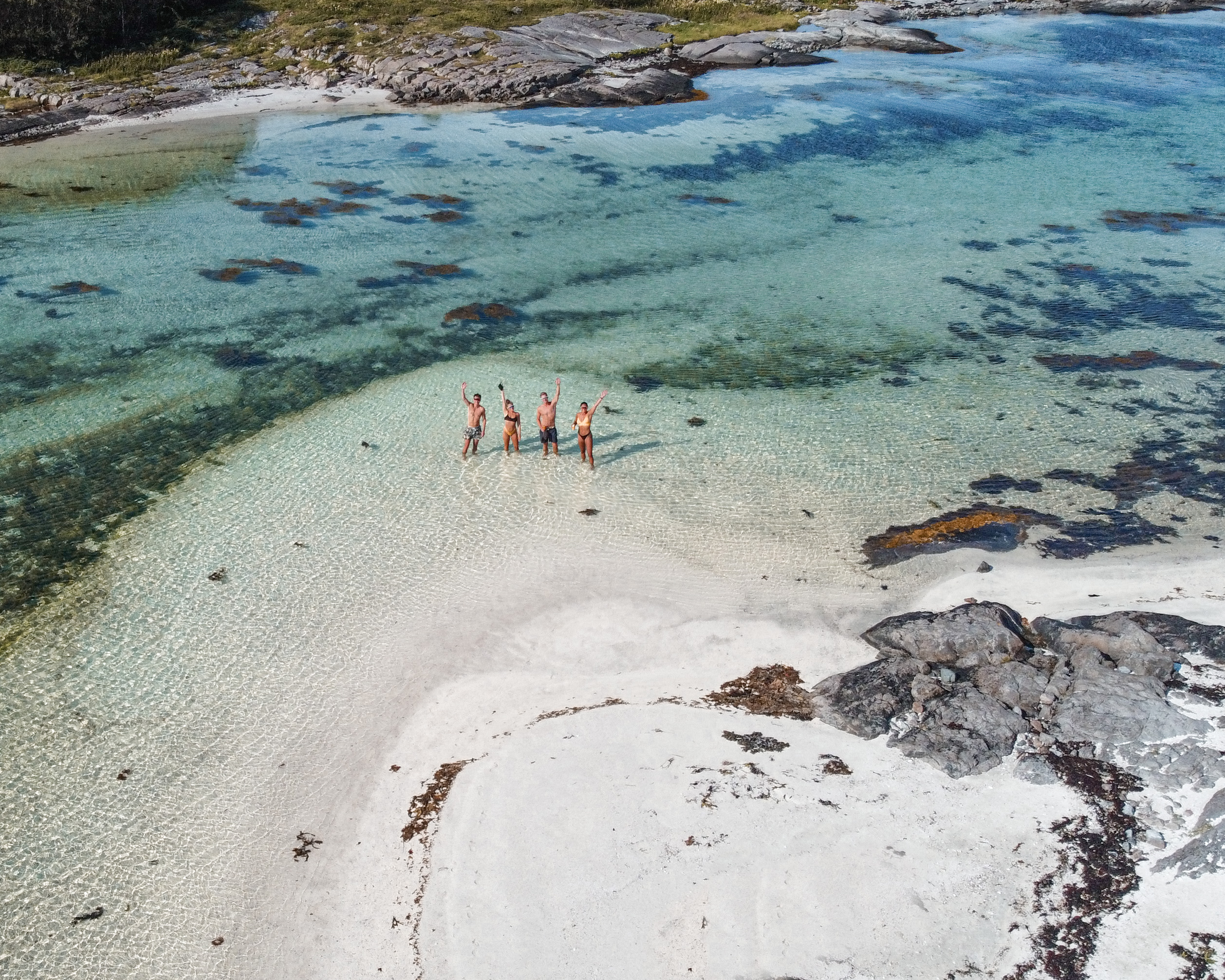 På bilden ser vi några som står i vattenbrynet i turkost vatten på ön Stött i Helgelands skärgård