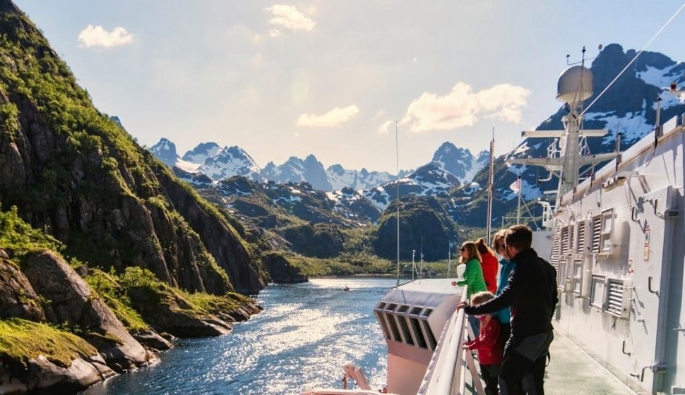 På bilden ser vi ett fartygsdäck från Hurtigrutbåten i Norge med utsikt över fjäll och fjord