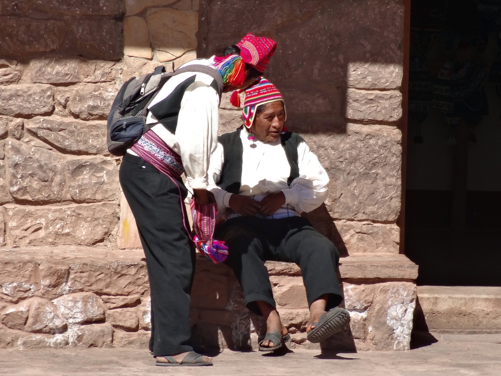 Två män med färggranna mössor, svarta byxor och vita skjortor på Taquiles i Peru